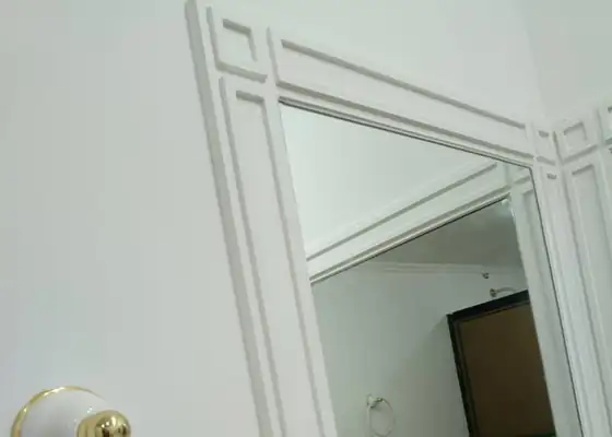 Detalhe da moldura branca de espelho com cabide dourado em banheiro, nos Jardins